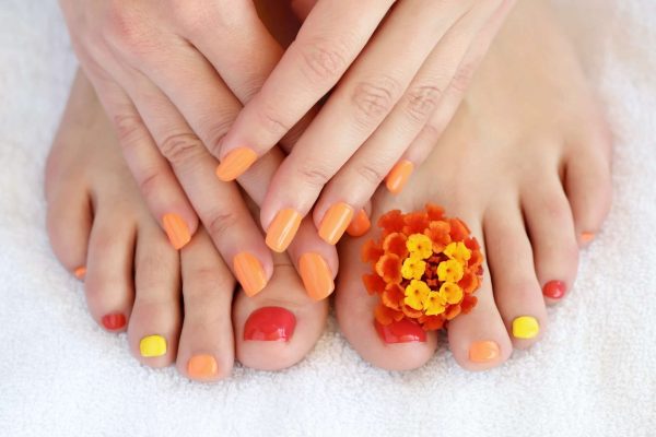 Female feet and hands with colorful manicure with red-orange flowers. Soft focus image